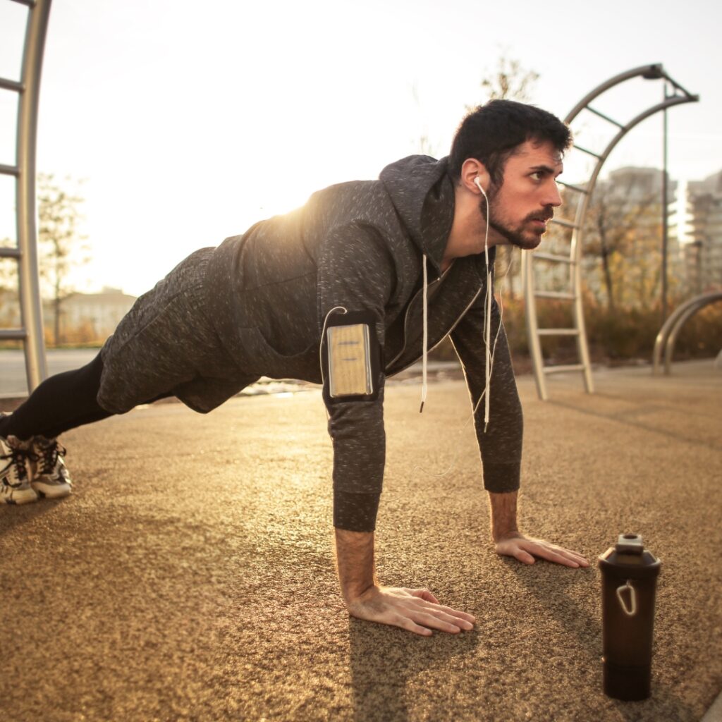 A man in a push-up position outdoors at sunset.