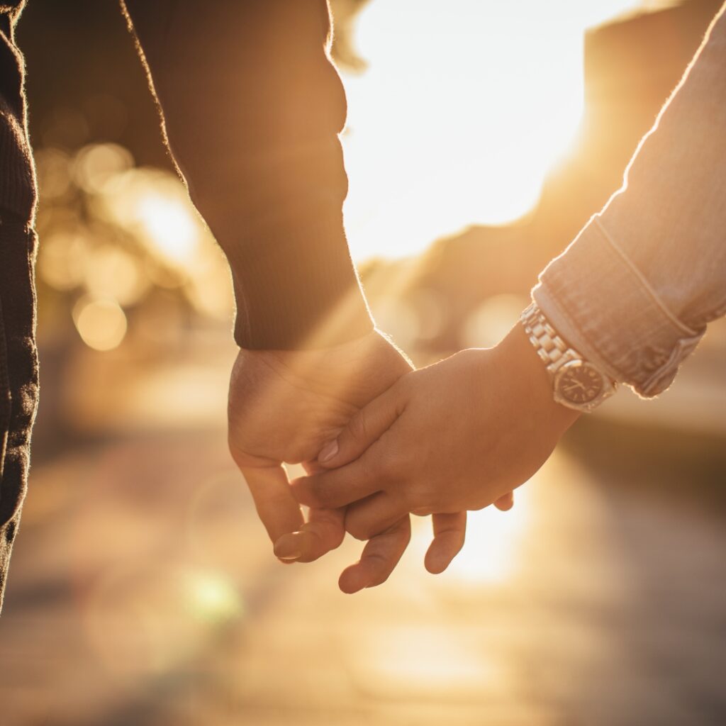 A close-up of two people holding hands with warm sunlight in the background.